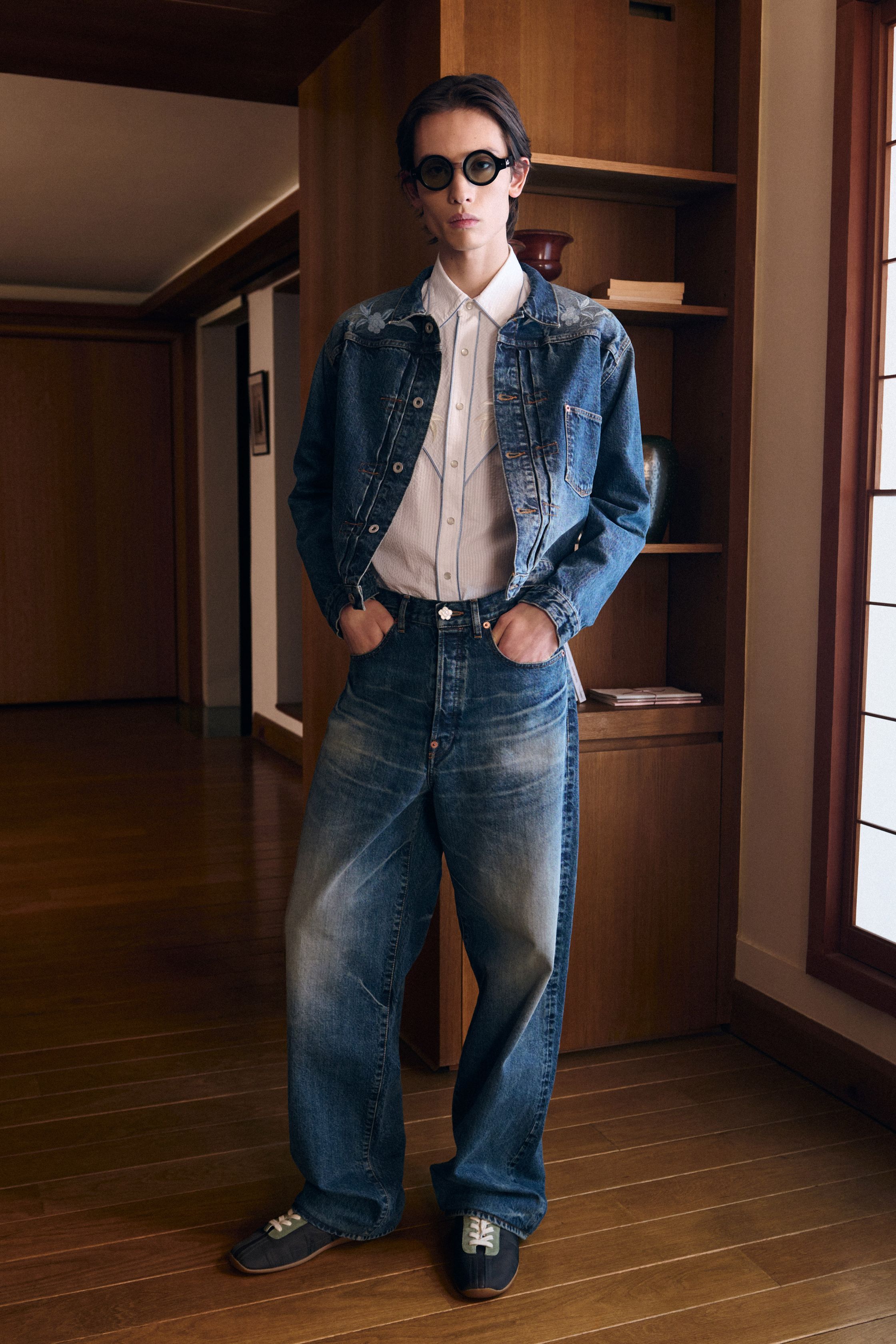 Kenzo 26FW 以“当代旅人”为核心叙事，将日式空间感、巴黎学院派与实穿丹宁重新缝合。剪裁不再强调街头张扬，而是回归比例与层次的节制美学：短外套、羊剪绒飞行夹克、衬衫式连衣廓形在柔光室内场景中显得克制而精准。整体色彩低饱和、结构干净，呈现出一种“被驯化的冒险精神”，让 Kenzo 从符号型街头回到高完成度的现代生活衣橱-顽石频道趋势研究